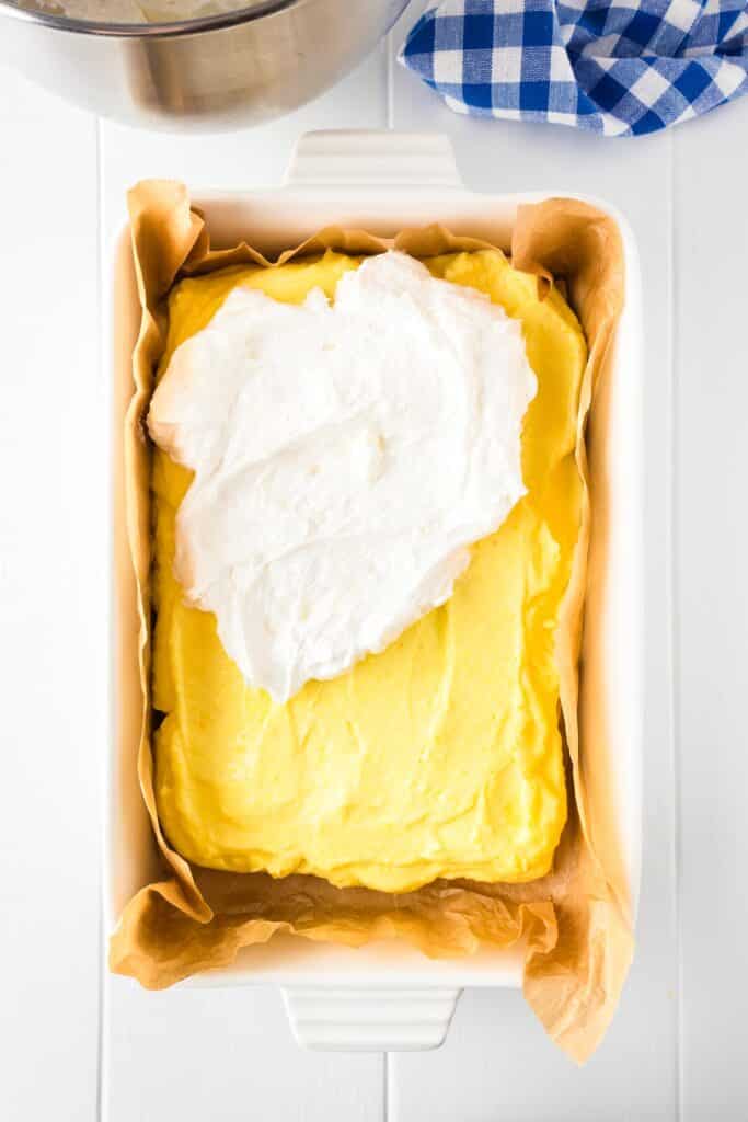 A baking dish with lemon pudding filling being topped with a layer of marshmallow cream for frozen lemon s'mores.