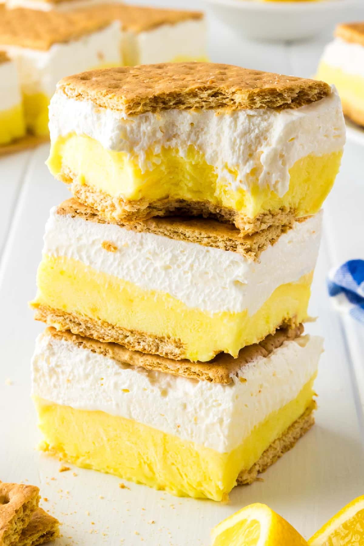 Stacked lemon icebox cake slices with layers of whipped cream and lemon filling with the top lemon smore missing a bite.