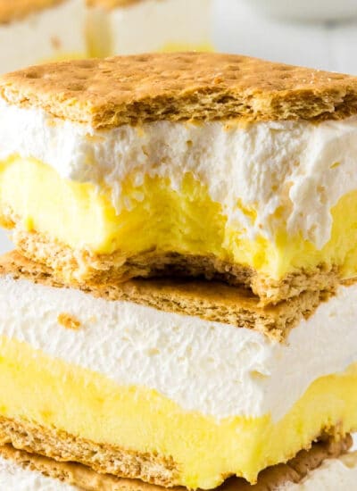 A close-up image of two layered frozen lemon s'mores ice cream sandwiches stacked with the top one missing a bite.