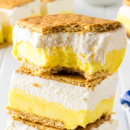 A close-up image of two layered frozen lemon s'mores ice cream sandwiches stacked with the top one missing a bite.