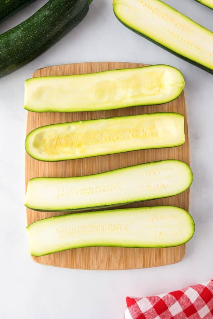 Four zucchini halves on a wooden cutting board, with two zucchini hollowed out.