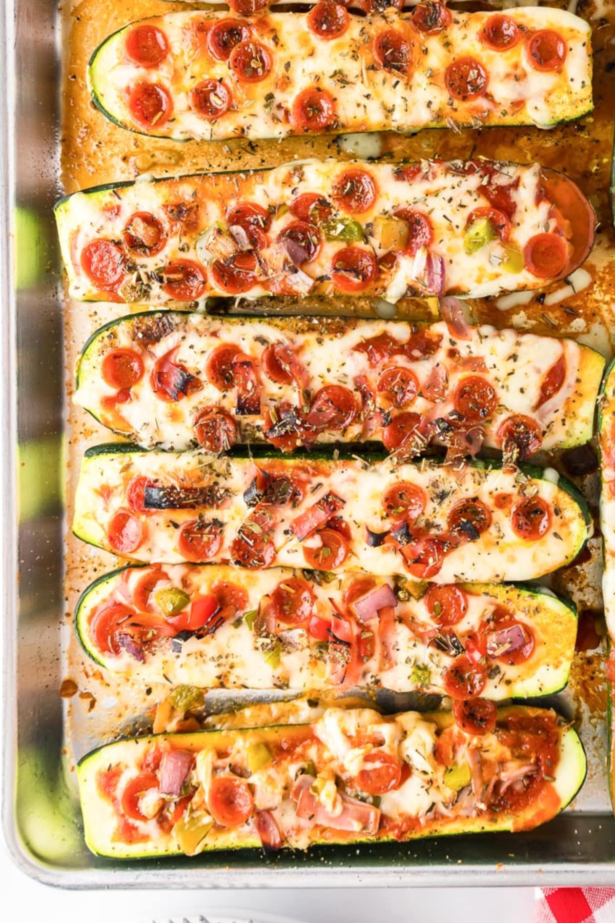 A tray of baked zucchini pizza boats topped with melted cheese, mini pepperoni slices, and various chopped vegetables.