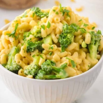 A bowl of macaroni and cheese mixed with pieces of broccoli, garnished with chopped herbs.