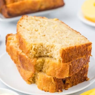 A close-up of two slices of banana bread on a white plate with a blurred loaf in the background.
