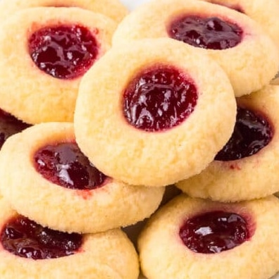 Close-up of a pile of round, golden thumbprint cookies filled with red jam.