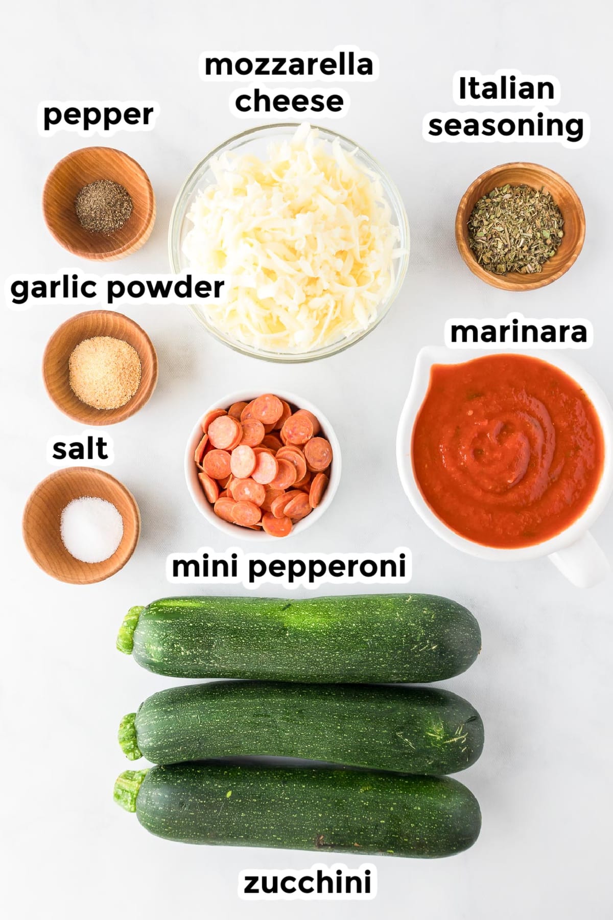 Ingredients for zucchini pizza boats in bowls with text labels.