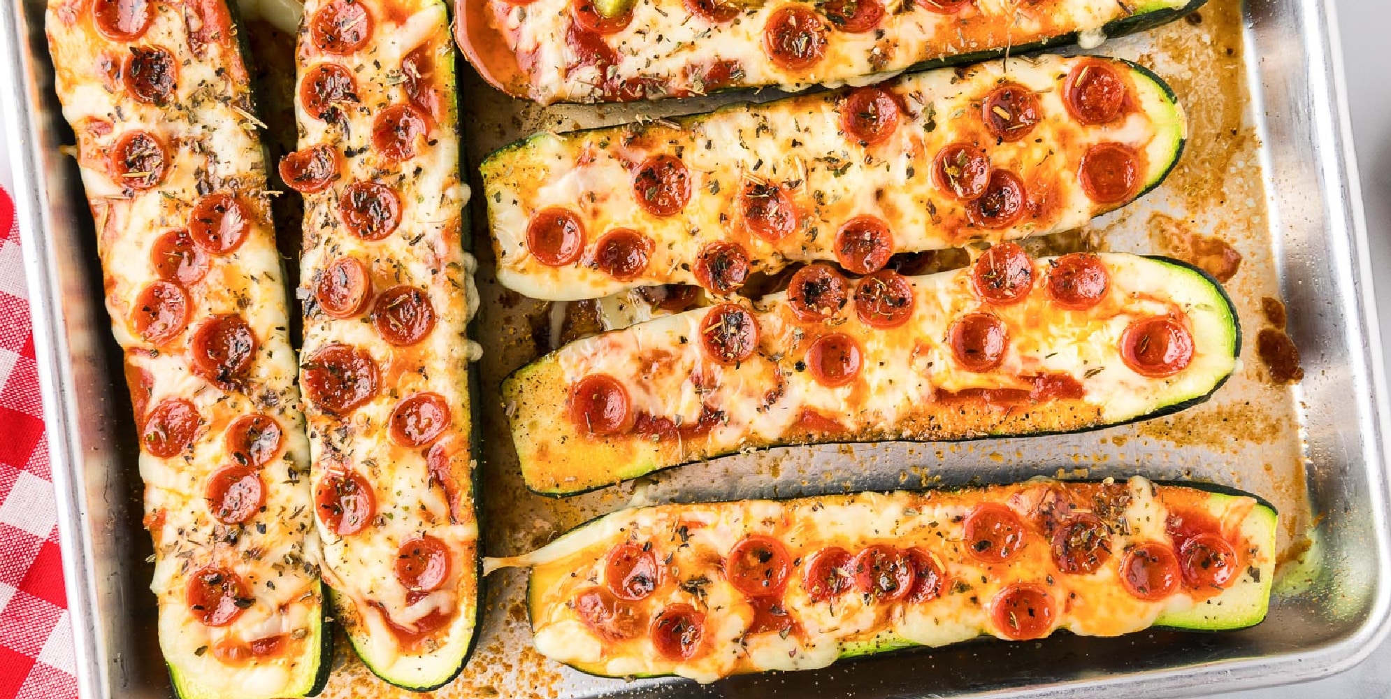 A tray of zucchini pizza boats topped with melted cheese and mini pepperoni slices on a pan.