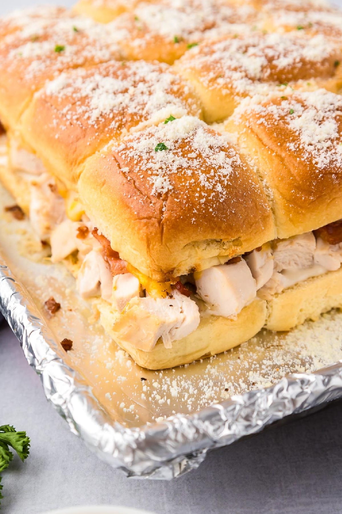 A tray of chicken bacon ranch sliders topped with parmesan cheese angled on a aluminum foil covered baking sheet.