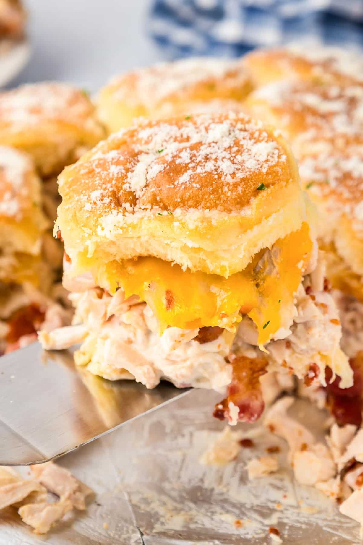 Close-up of a chicken bacon ranch slider with gooey melted cheese being served with a metal spatula.