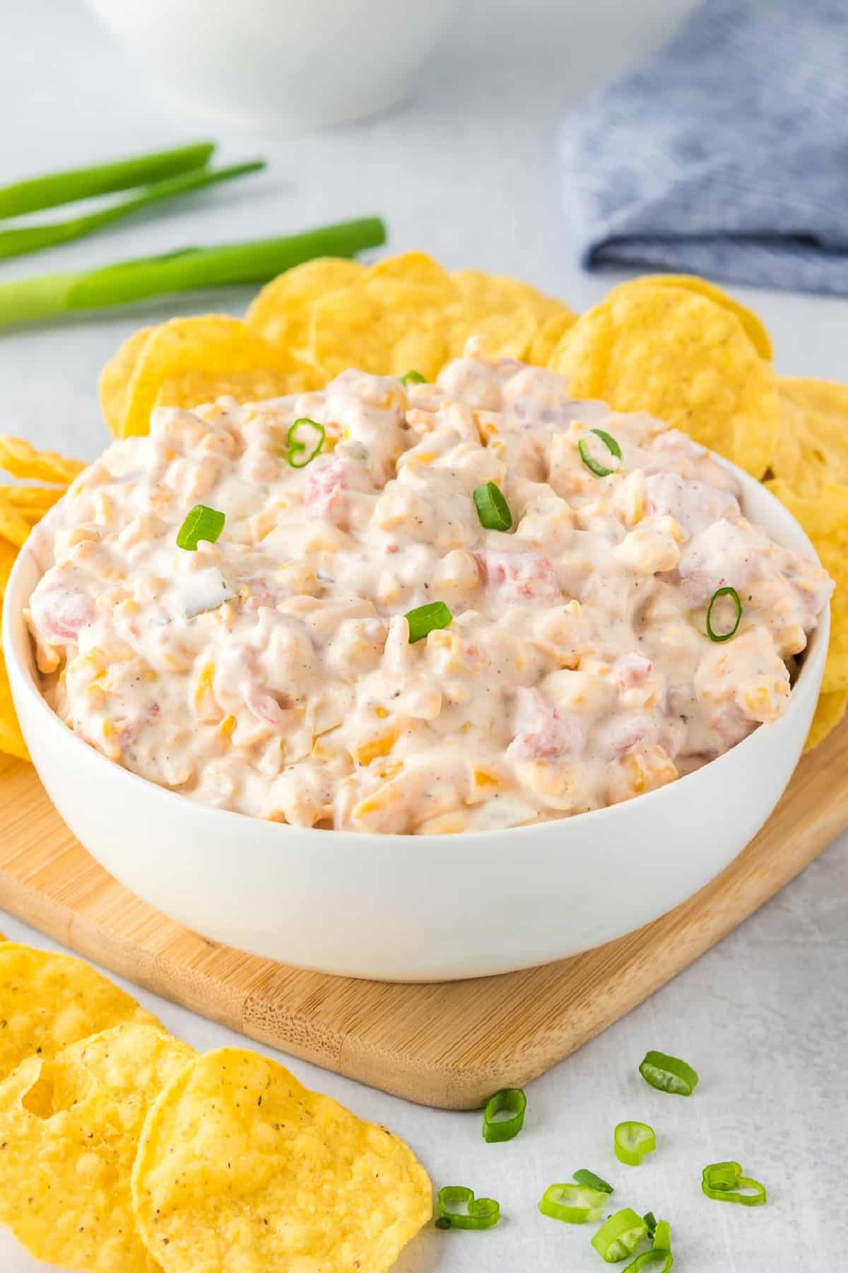 A white bowl filled with a creamy corn dip with rotel from the side surrounded by tortilla chips.