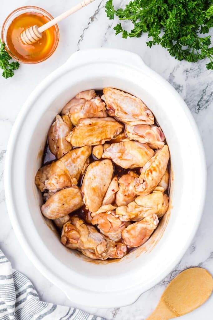 A slow cooker filled with raw chicken wings coated in bbq sauce on a counter.