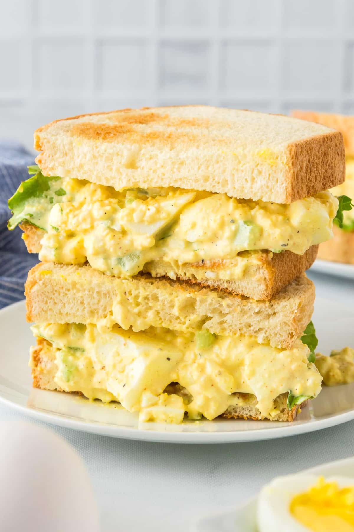A plate with an egg salad sandwich cut into two pieces stacked on top of each other.