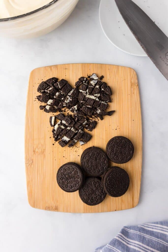 A wooden cutting board with whole cookies at the bottom and chopped Oreo cookies at the top.