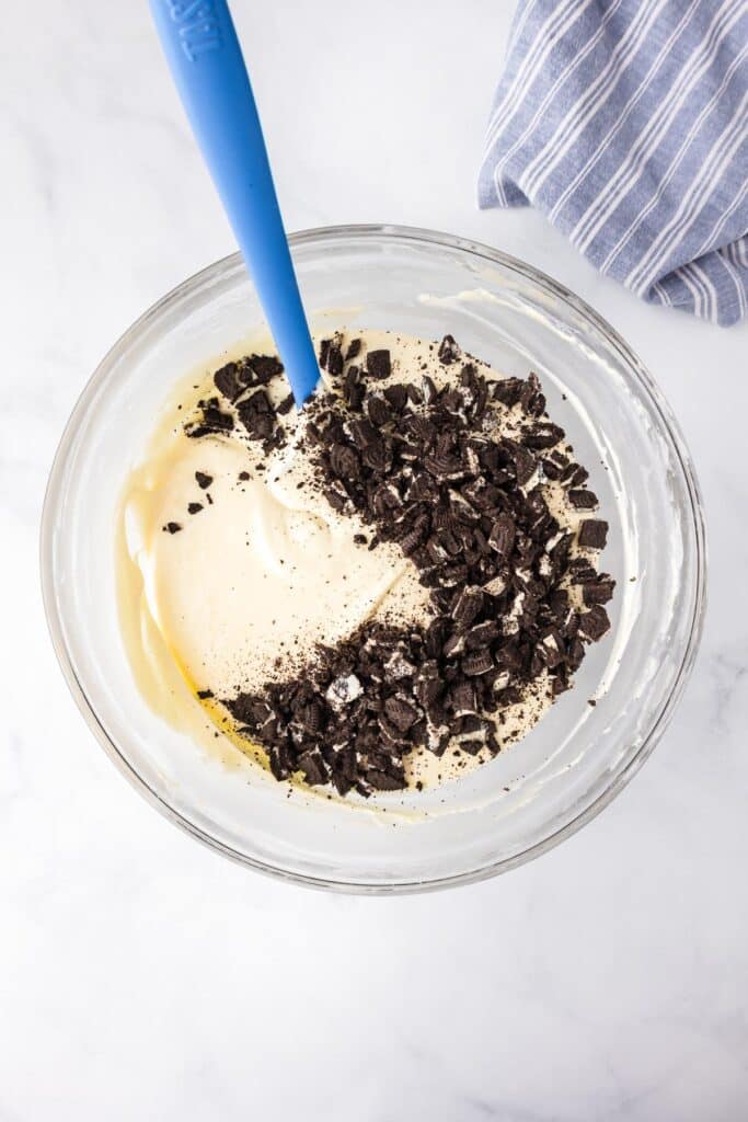A mixing bowl containing a cream cheese mixture with Oreo cookie crumbles being folded in.