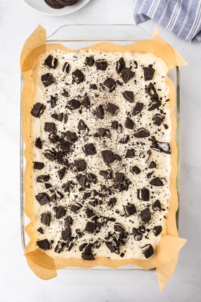 Oreo cheesecake bars in a parchment lined glass pan right before baking.