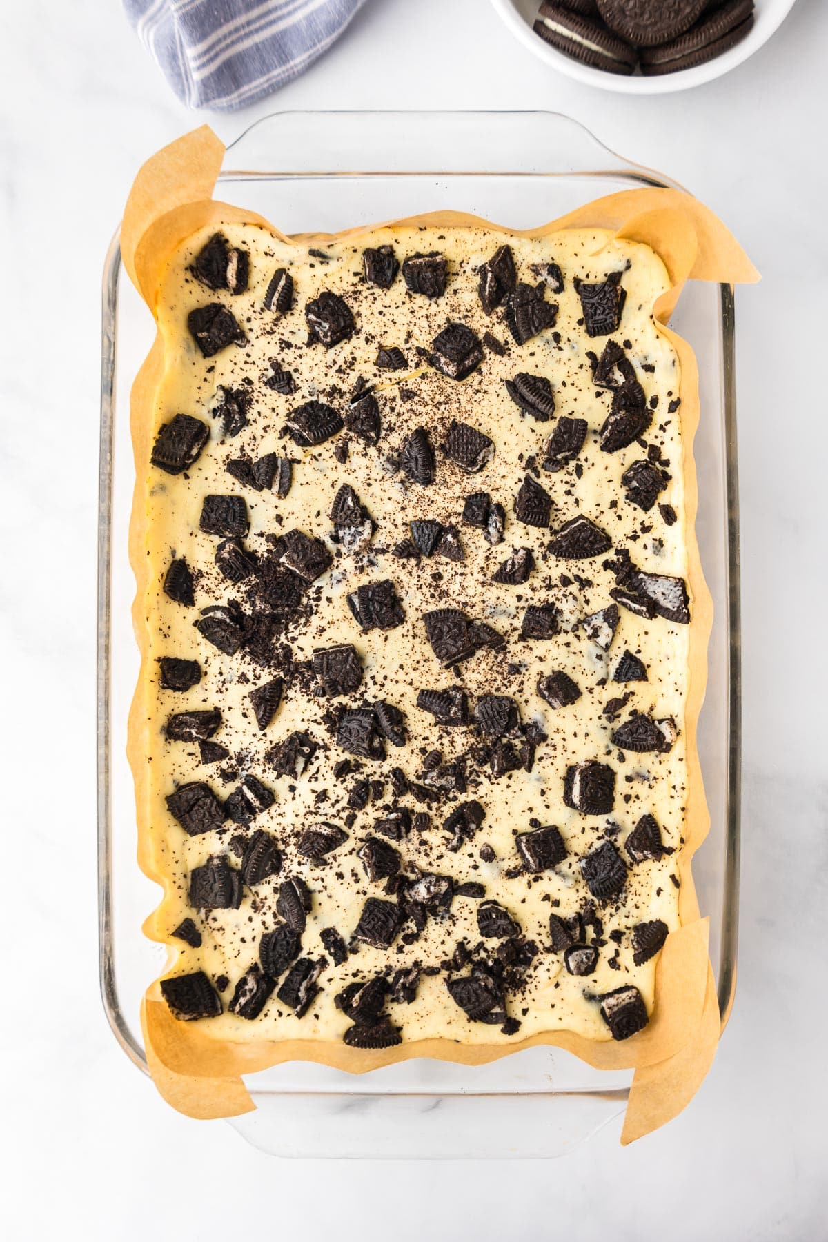 Oreo cheesecake bars in a parchment lined glass pan after baking.