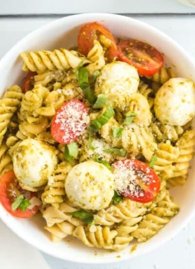 A bowl of pesto pasta salad with cherry tomatoes, mozzarella cheese pieces and shredded basil.