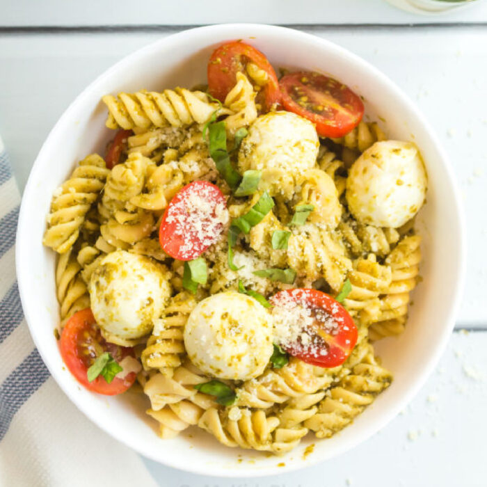 A bowl of pesto pasta salad with cherry tomatoes, mozzarella cheese pieces and shredded basil.