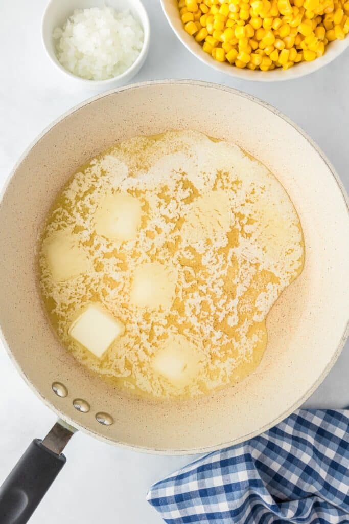 A skillet filled with melting butter, with onion and corn in bowls nearby.