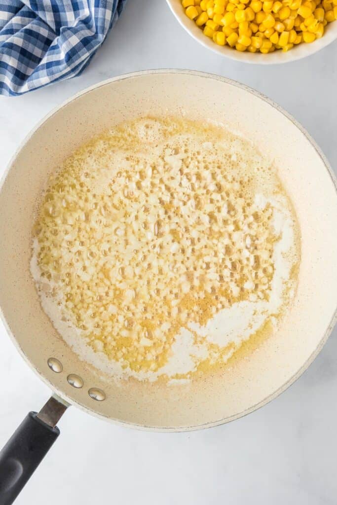 A skillet with diced onion cooking in butter with corn in a bowl nearby.