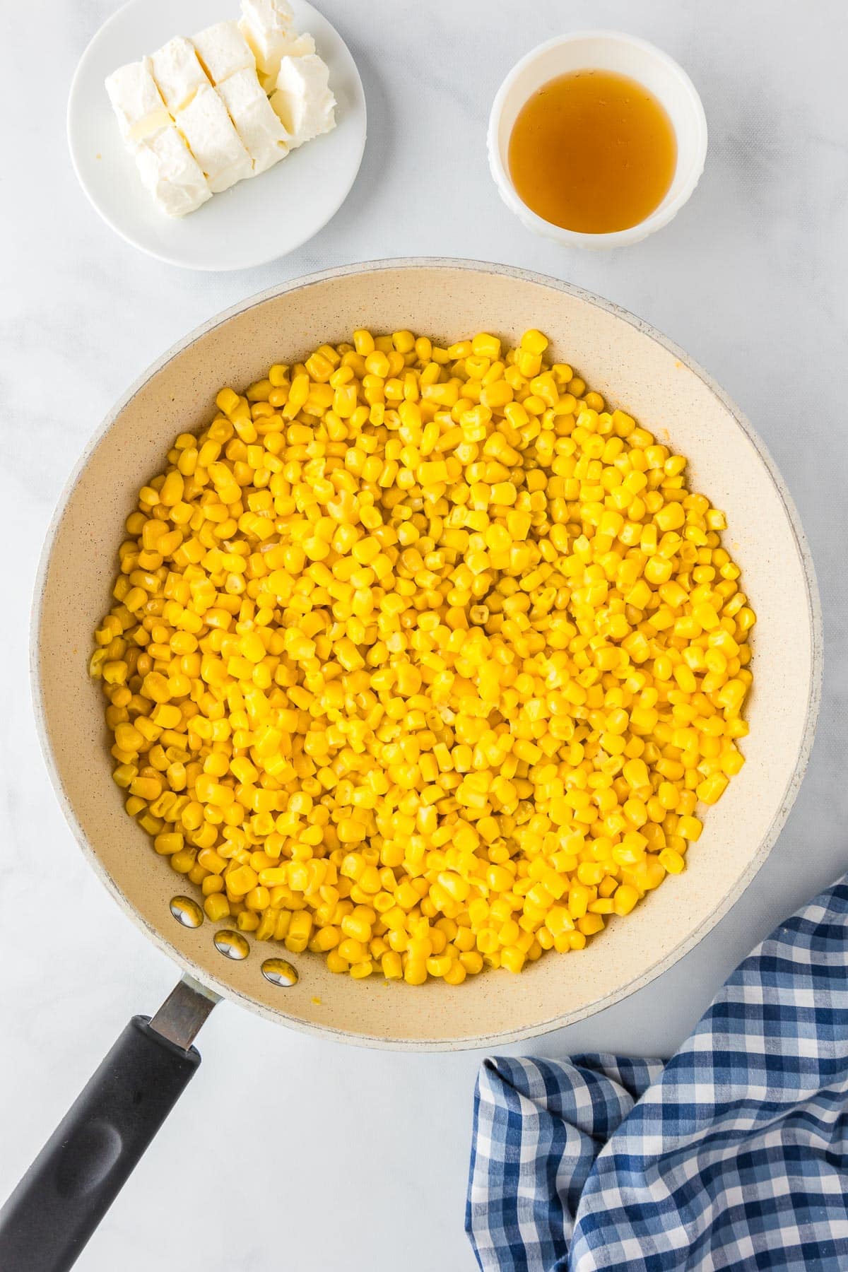 A pan filled with cooked corn kernels with cream cheese and honey in bowls nearby.