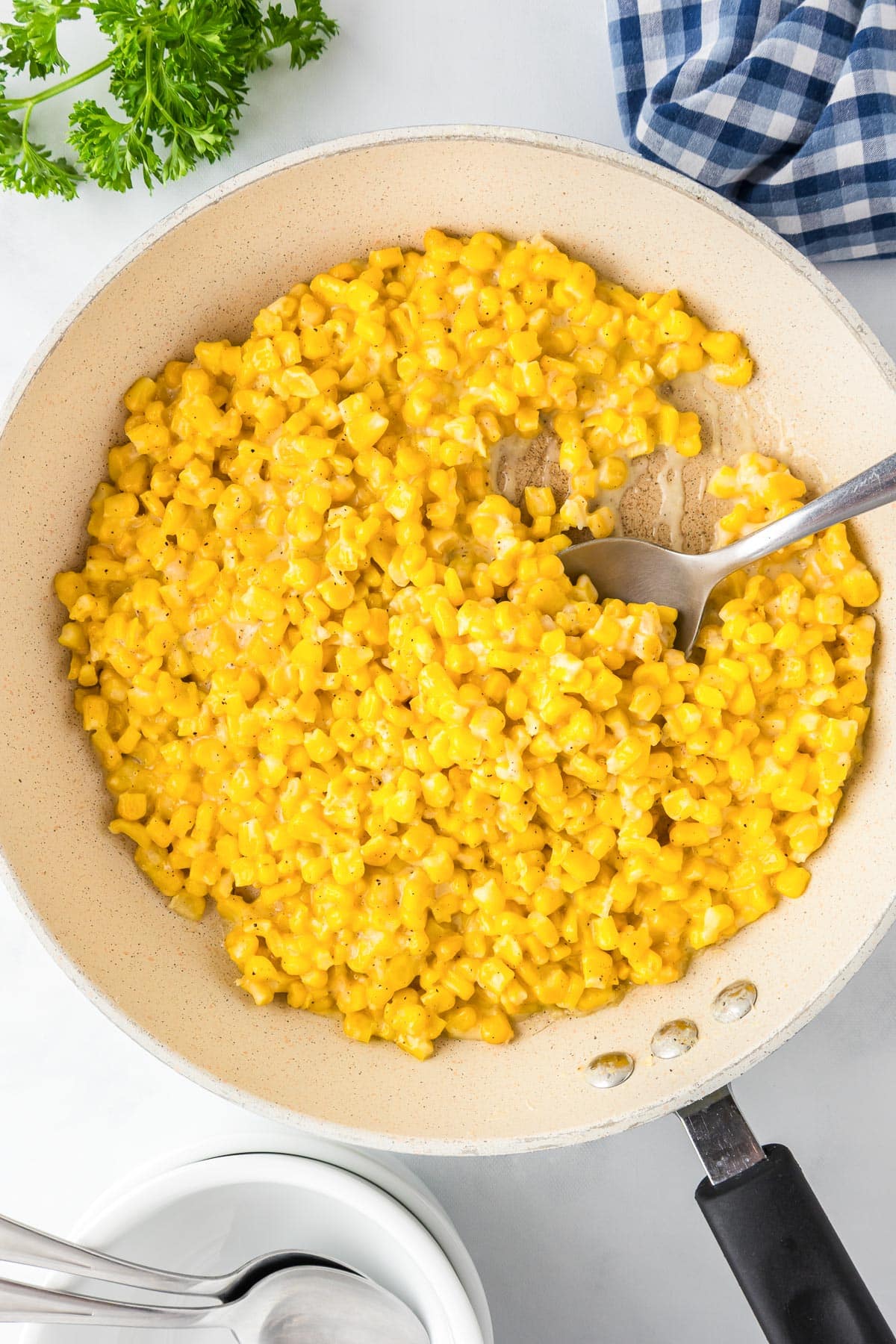 A pan filled with creamy skillet honey butter corn kernels in a pan being scooped with a serving spoon.