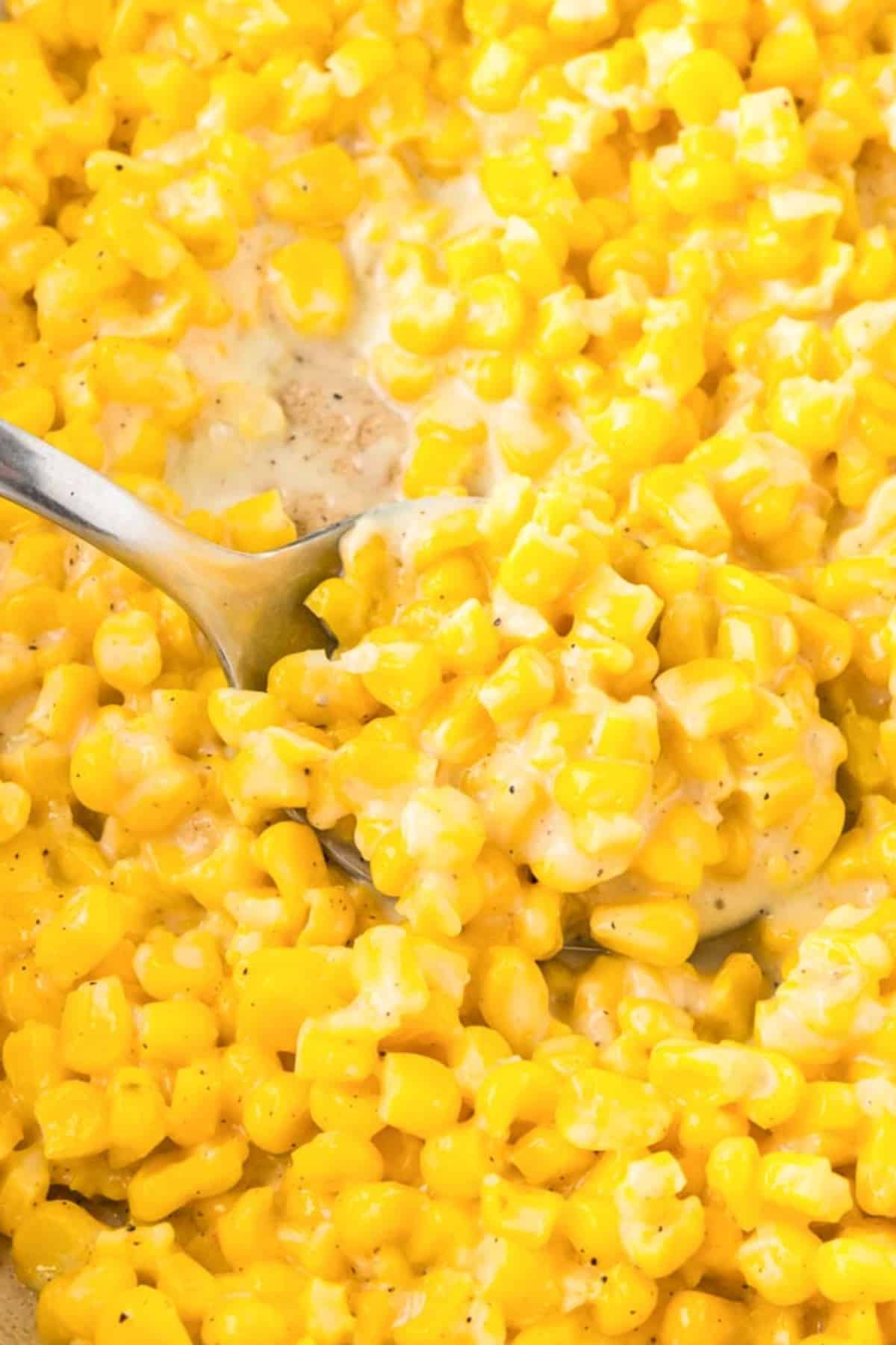 A close-up of a spoon scooping creamy skillet honey butter corn mixed with seasoning.