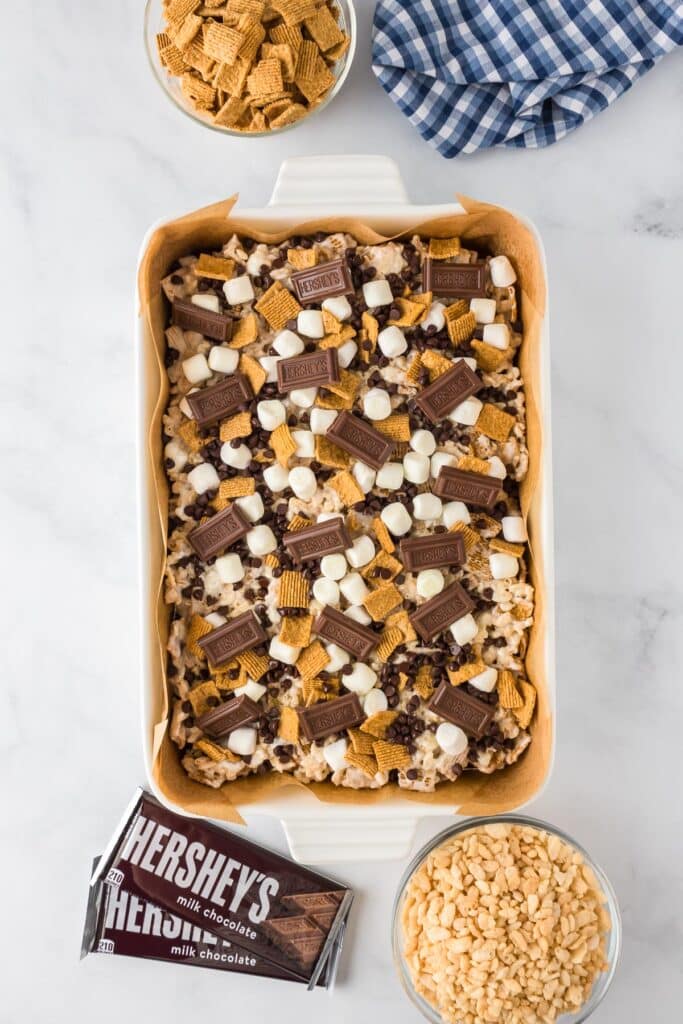A baking dish with s'mores Rice Krispies treats topped with mini marshmallows, Hershey's chocolate pieces, mini chocolate chips and Golden Grahams pieces.