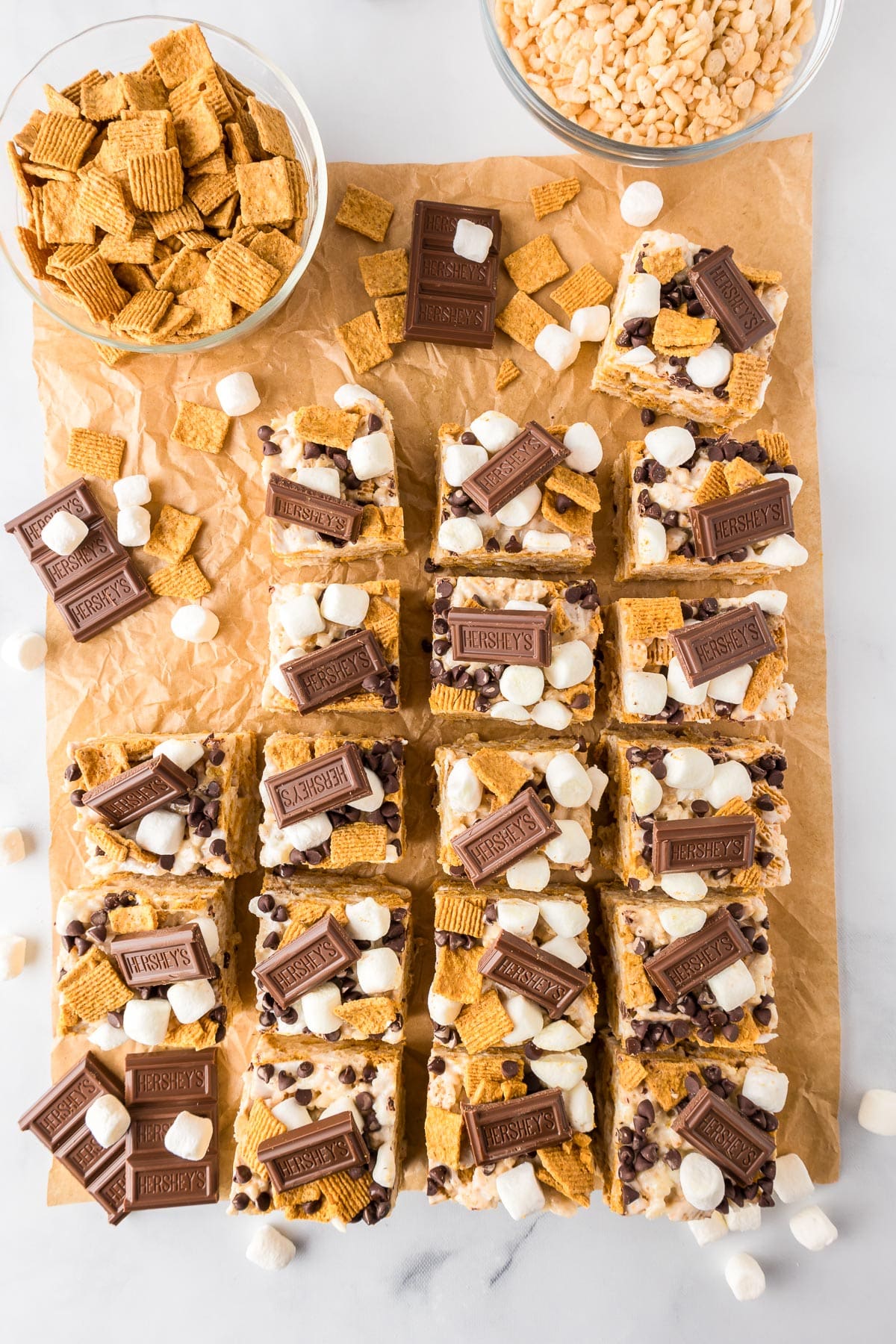 A tray of s'mores bars cut into squares, topped with mini marshmallows, chocolate pieces, and cereal from overhead on parchment paper.
