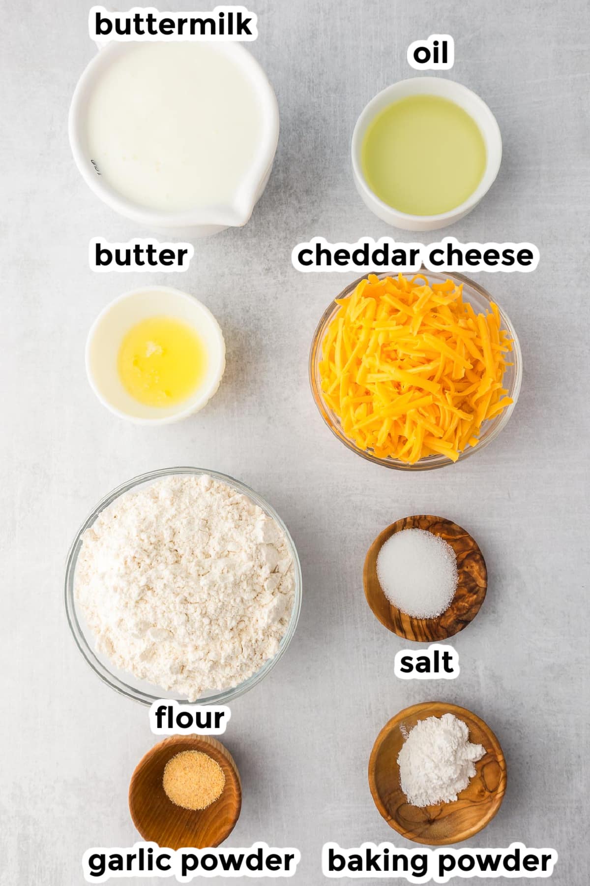 Ingredients for cheddar garlic biscuits in bowls on a counter with title text labels.