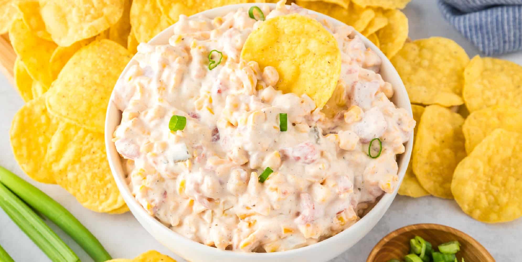 A bowl of creamy corn dip with Rotel garnished surrounded by tortilla chips.