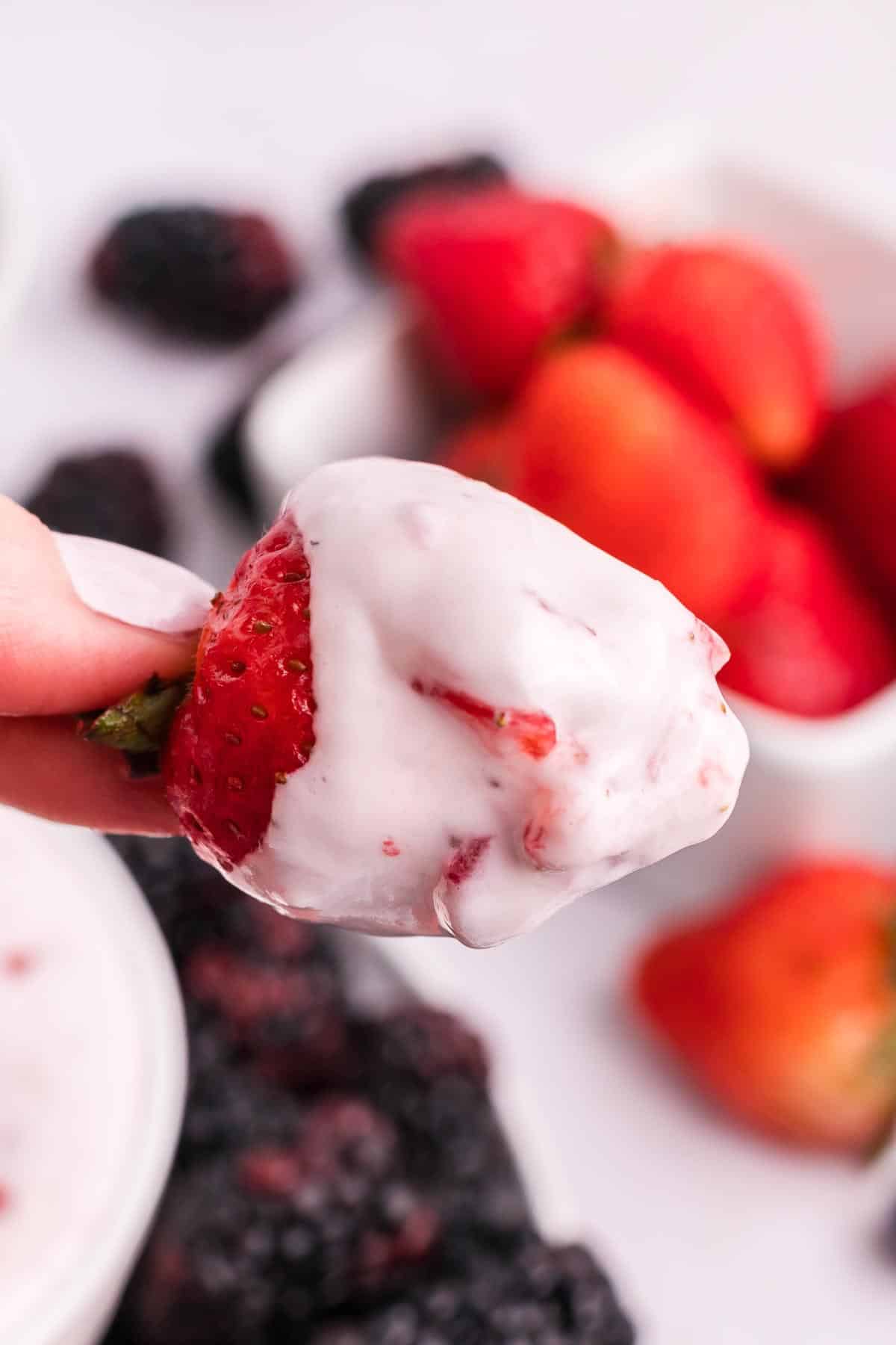 A hand holding a strawberry dipped in cream cheese fruit dip.