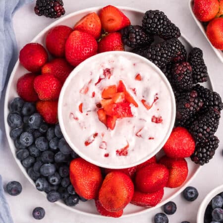 Square view of a cream cheese fruit dip topped with strawberry bits and surrounded by a platter of berries to dip.