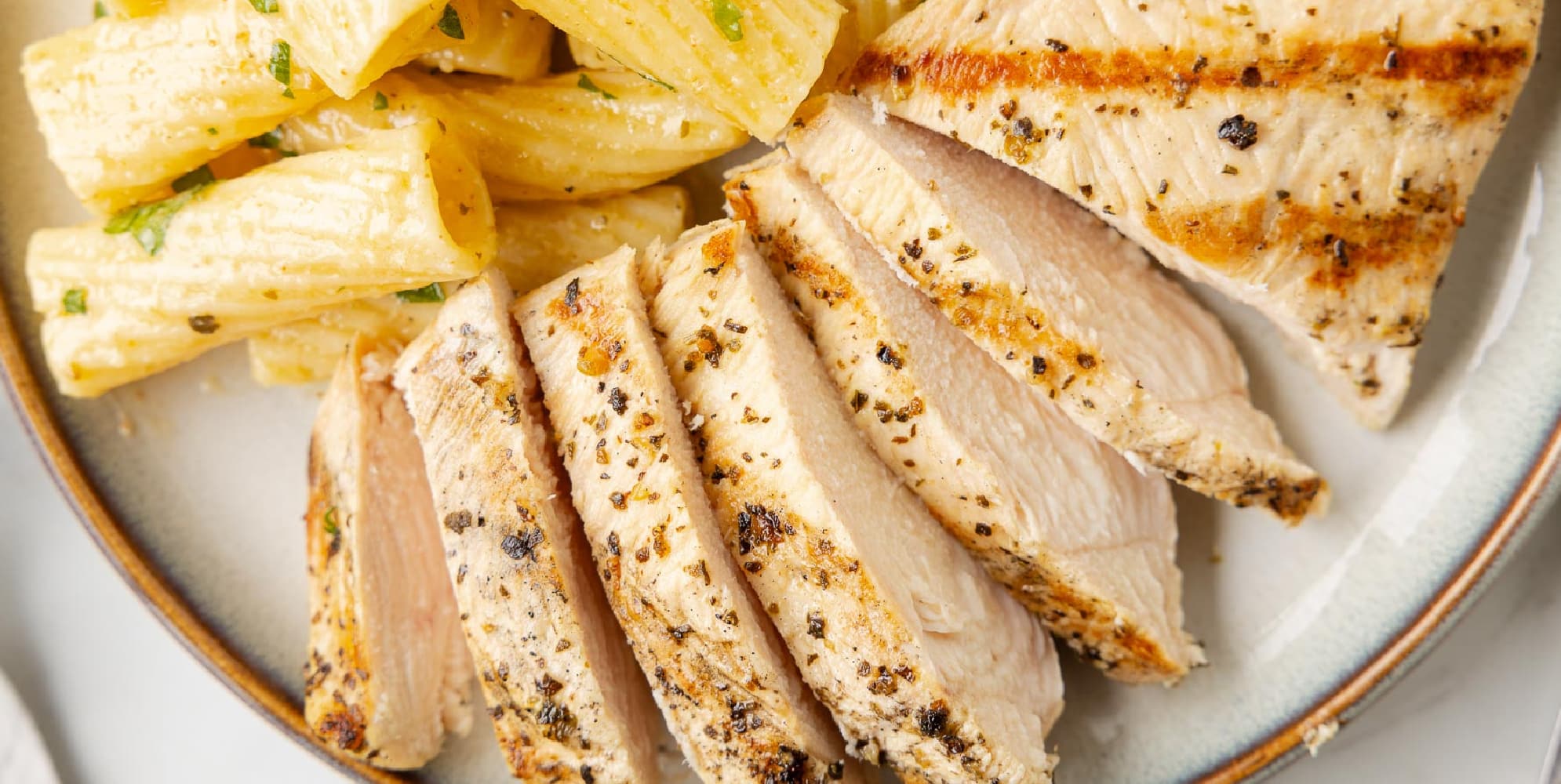 A plate with seasoned and sliced grilled Italian chicken breast paired with pasta on a plate.