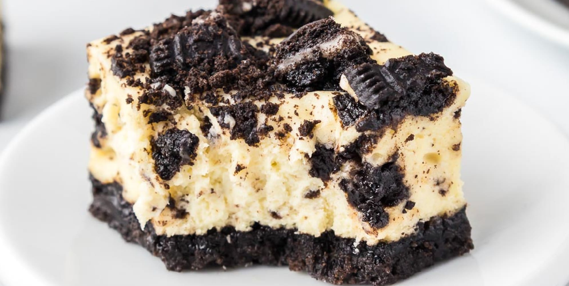 A close-up wide view of an Oreo cheesecake bar topped with Oreo cookie pieces with a bite missing.