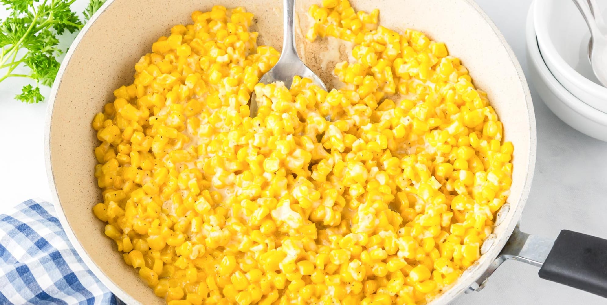 Wide view of a skillet filled with creamy honey butter corn, with a serving spoon scooping creamy corn in the middle.