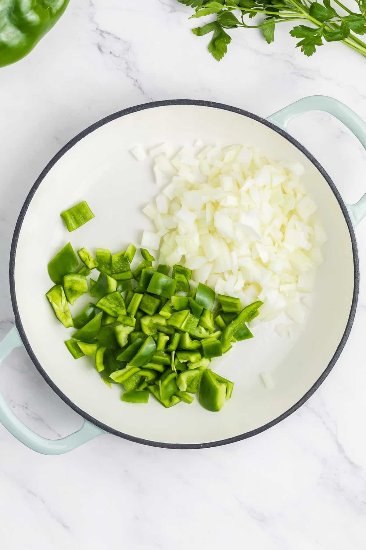 Chopped green bell peppers and onions in a white pan being cooked.