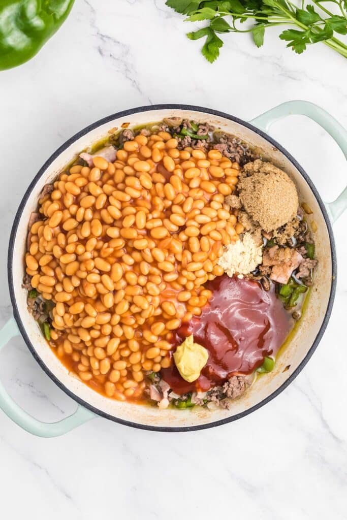 Large pot containing baked beans, ground beef, green bell pepper, brown sugar, mustard, ketchup, and minced garlic.