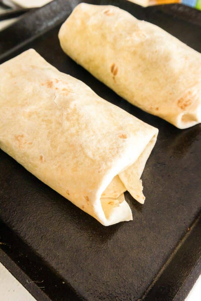 Two burritos placed side by side on a black pan being seared.