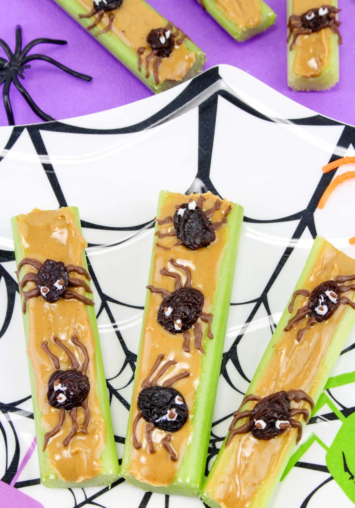 Celery sticks with peanut butter topped with raisin "spiders" decorated to look like spiders with chocolate on a Halloween plate.