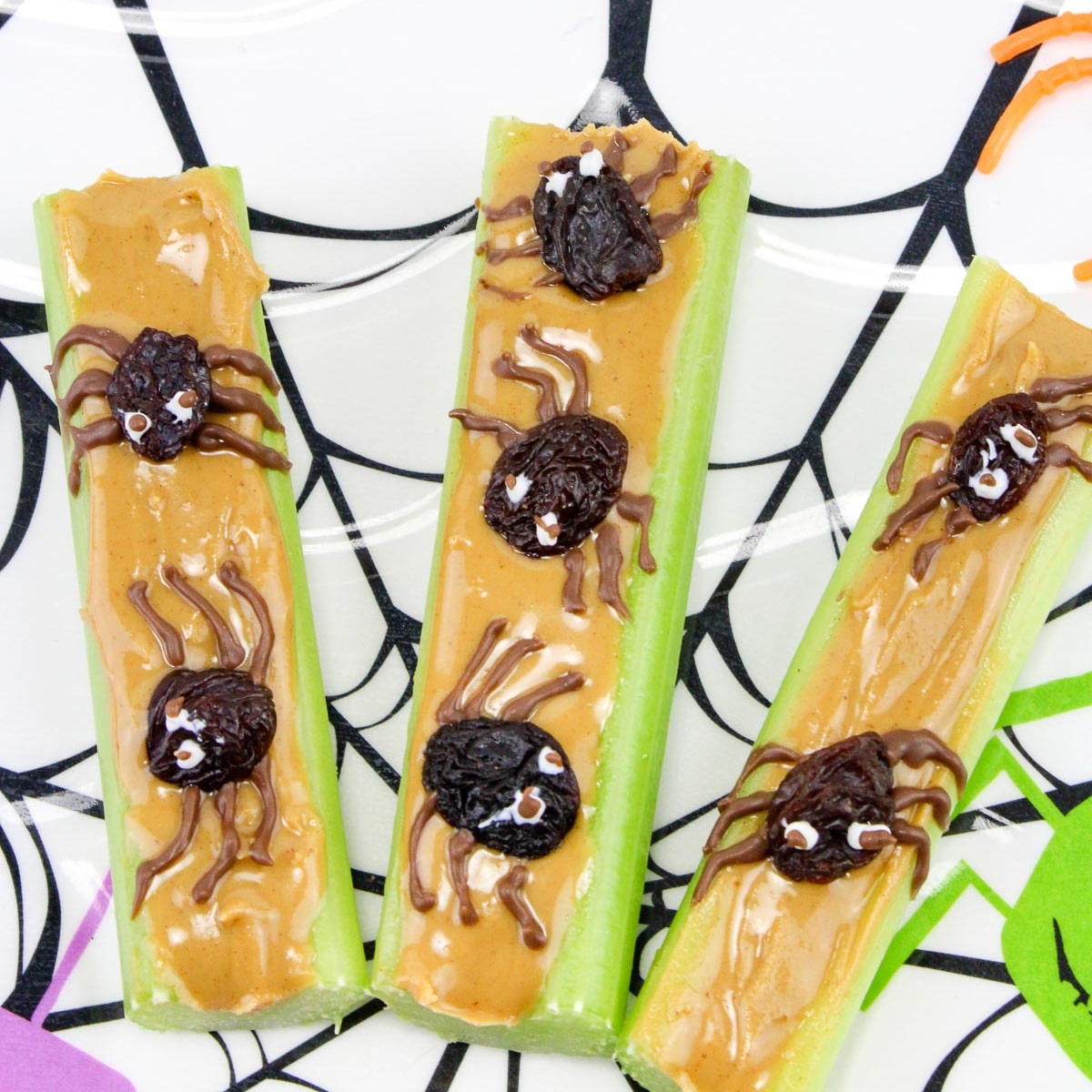 Celery sticks topped with peanut butter and raisins decorate with chocolate to look like spiders up close on a Halloween plate.