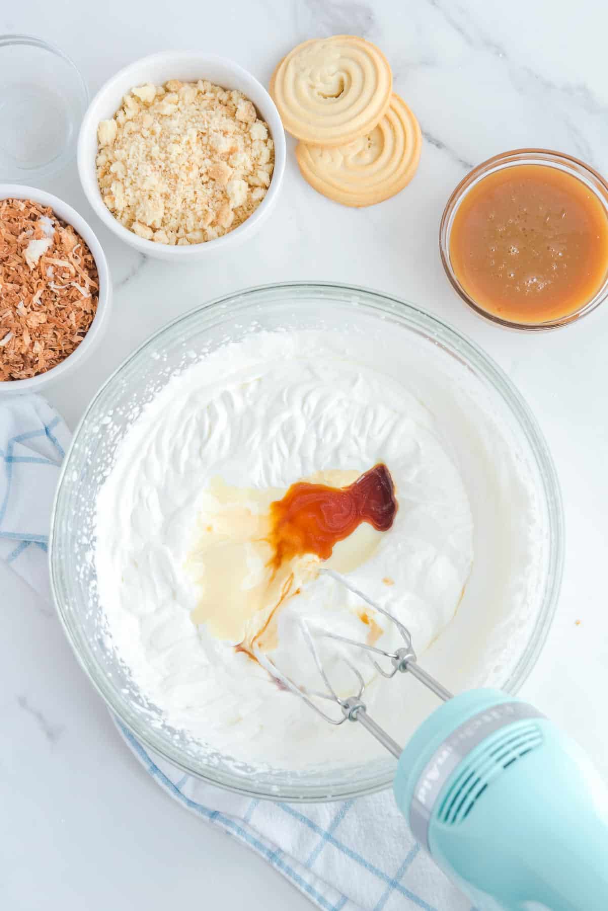 A mixing bowl with whipped cream. sweetened condensed milk, and vanilla being mixed into the whipped cream