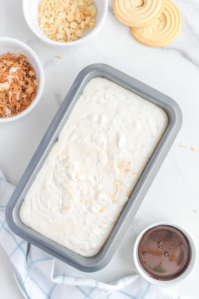 A bread pan filled with samoa ice cream mixture surrounded by more samoa cookie toppings.