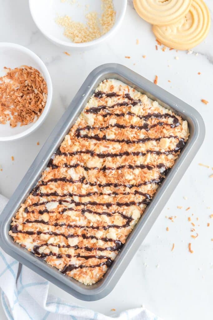 A bread pan filled with samoa ice cream mixture topped with coconut and drizzled with chocolate sauce.