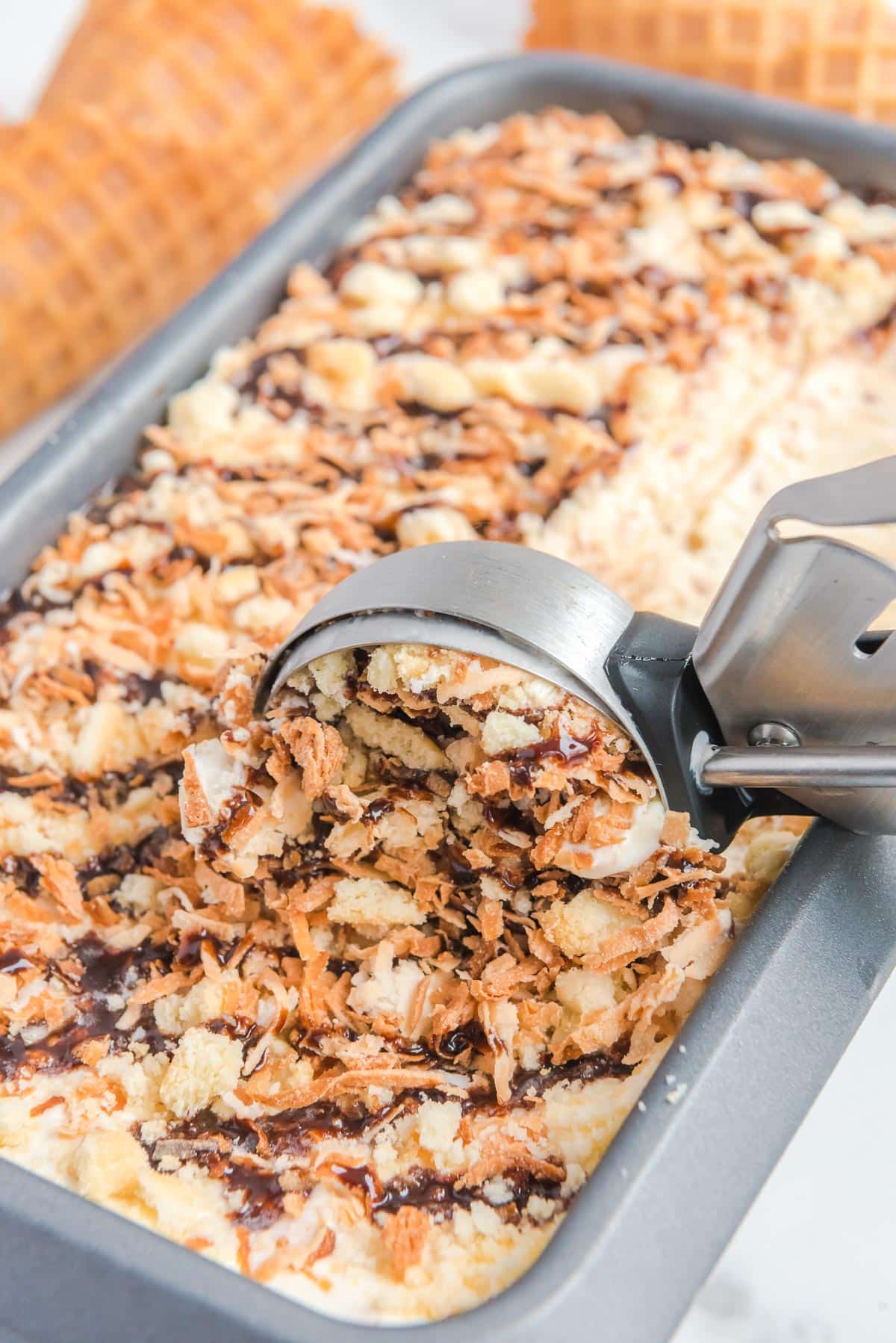 A metal ice cream scooping a portion of Samoa ice cream from a bread pan.