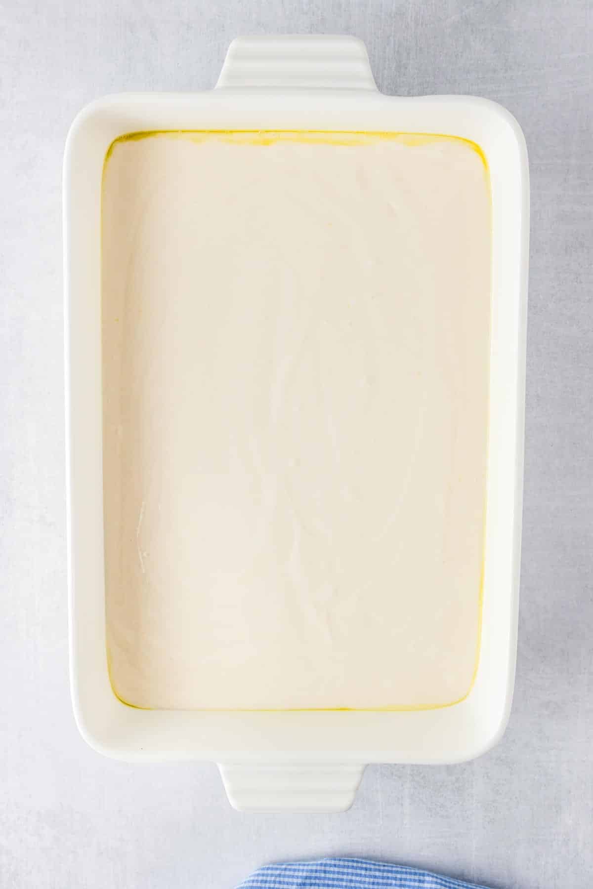 A rectangular white baking dish filled with unbaked white cake batter.