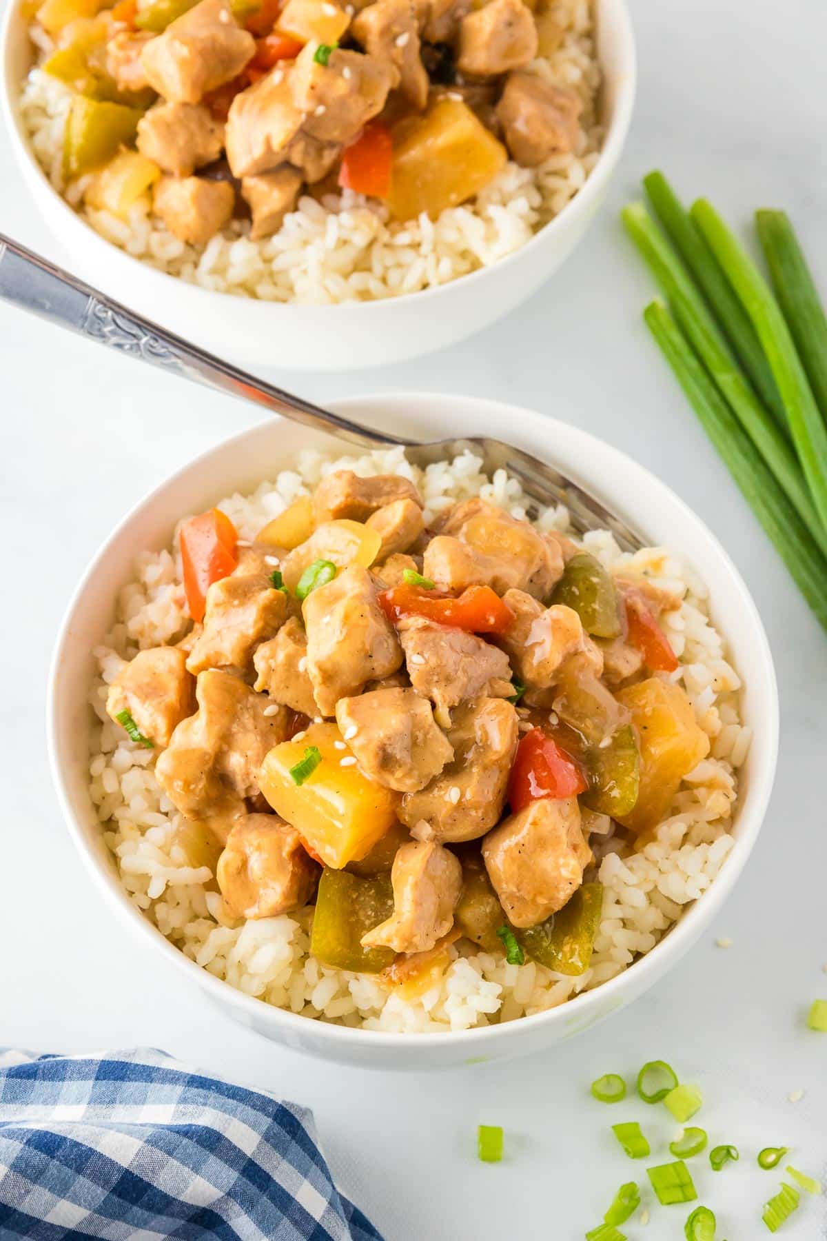 Two bowls of rice topped with sweet and sour pork, pineapple and peppers.