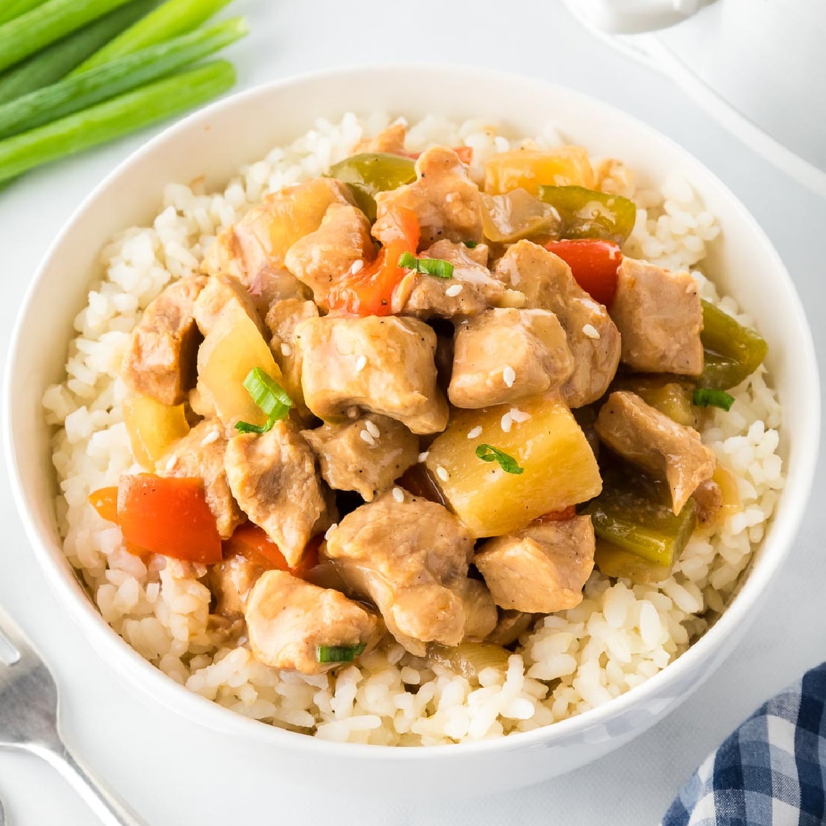 A bowl of rice topped with stir-fried pork, bell peppers, and pineapple chunks, garnished with sesame seeds and chopped green onions, reminiscent of the flavors found in pork lettuce wraps.