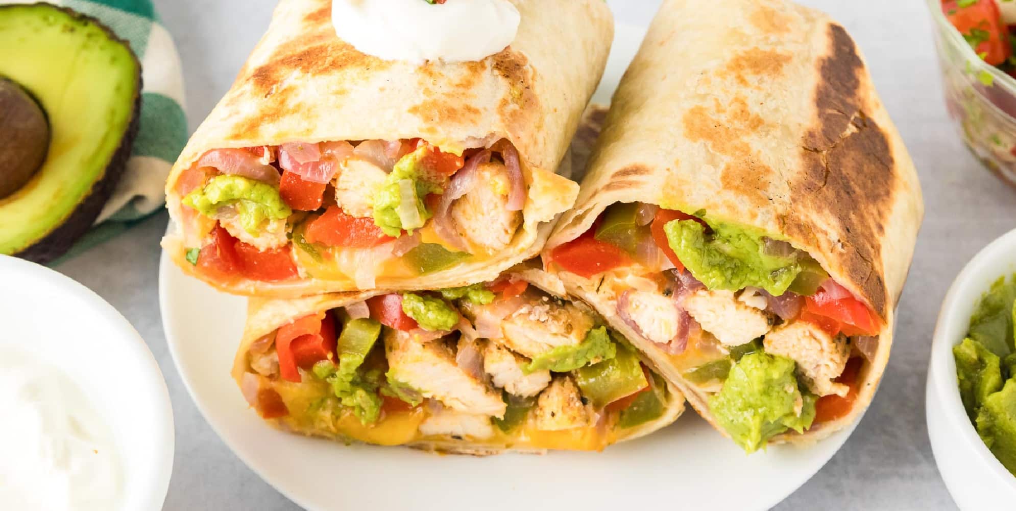 Wide view of three chicken fajita wraps stacked on a plate cut in half to see the filling.