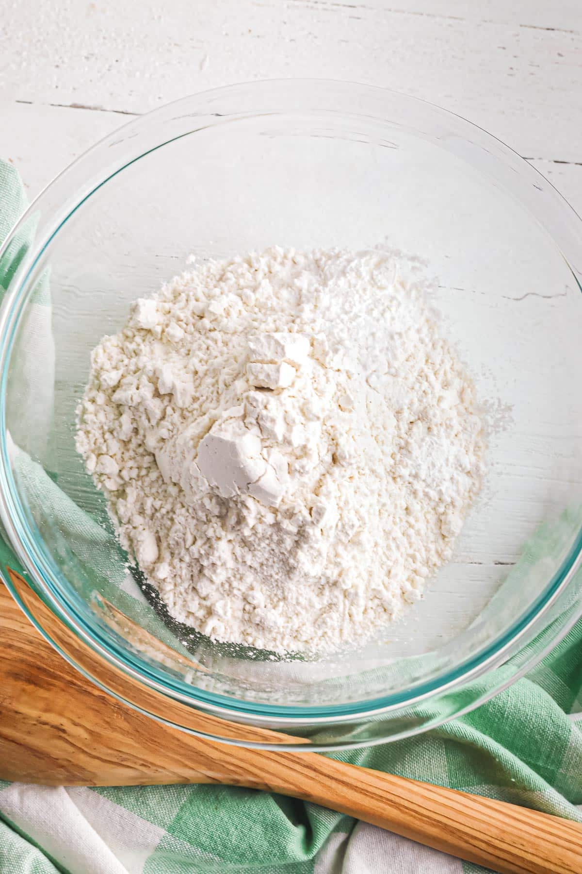 A clear glass bowl containing a mixture of dry ingredients including flour, baking soda, cornstarch and salt being mixed for chocolate chip toffee cookies.